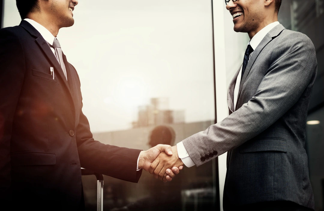 Two professionals shaking hands in an office, symbolizing strategic business partnerships.