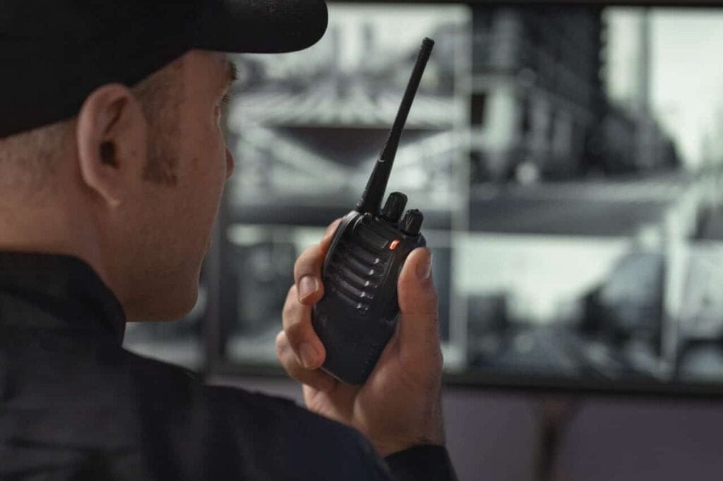 Security personnel using a walkie-talkie while monitoring surveillance footage to prevent equipment loss and theft.