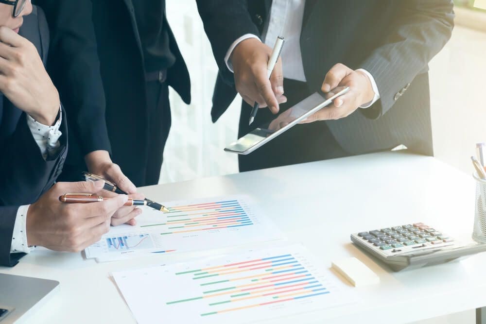 Three professionals discussing business plans at a table with documents and graphs.