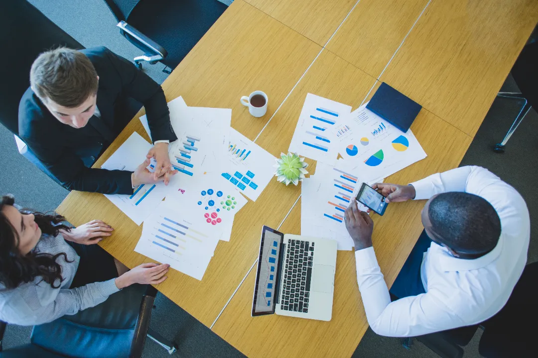 A team analyzing charts and documents during a market research discussion at a wooden table