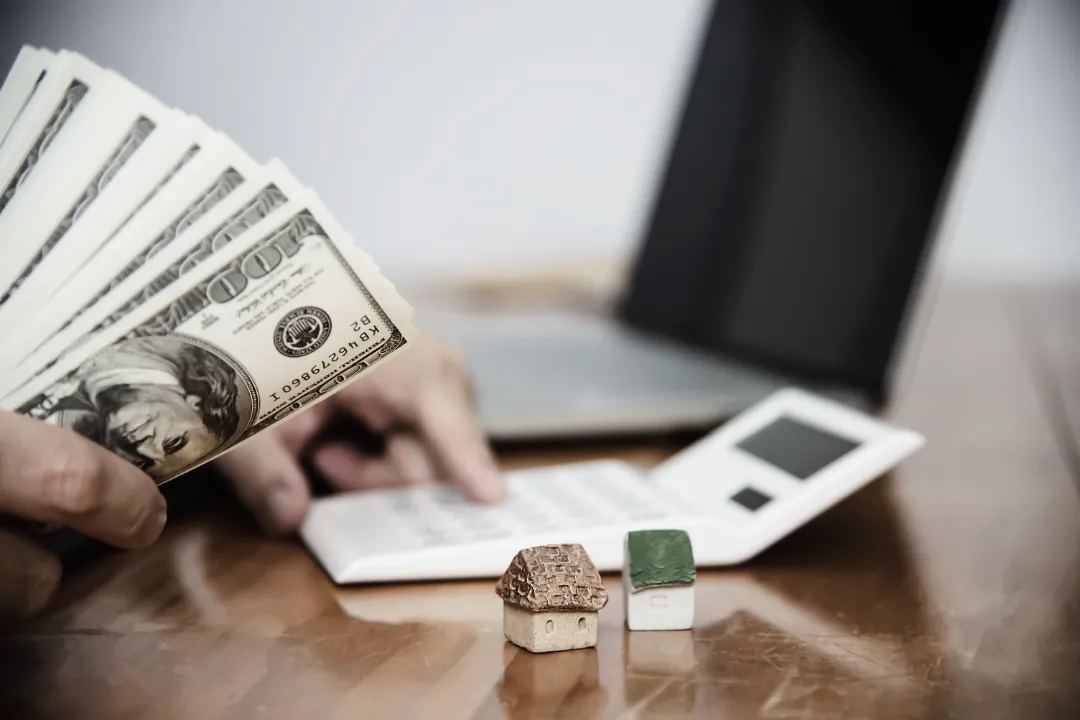 Close-up of money, calculator, and miniature houses symbolizing rental income