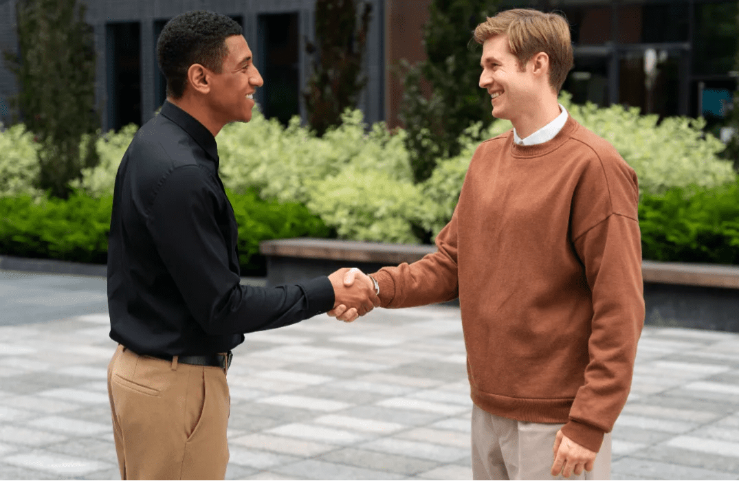 Two men shaking hands outdoors, smiling and making a business agreement.