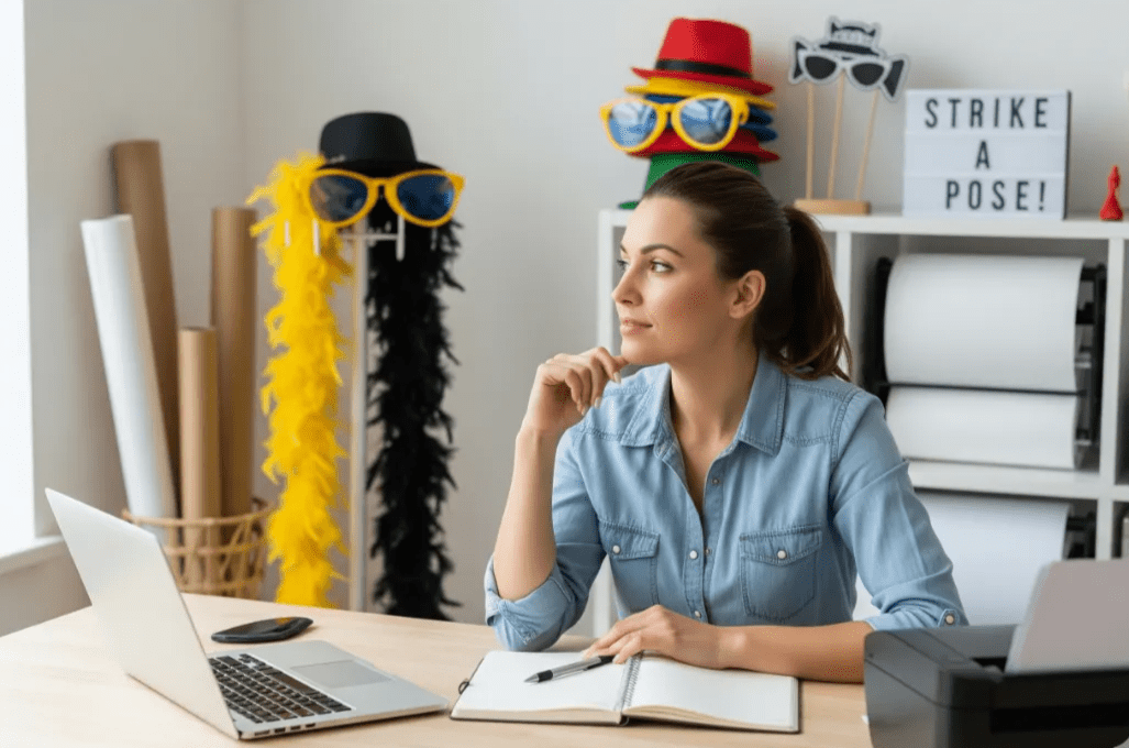 Photo booth business owner considering options with laptop and props nearby.