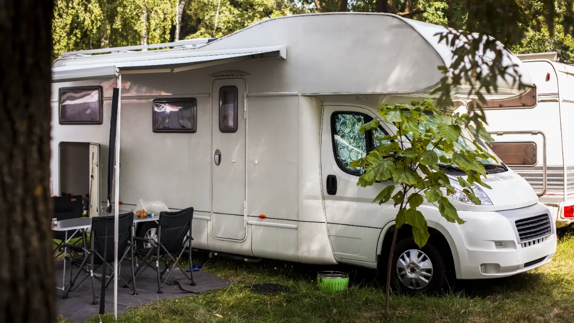 Class C motorhome parked at campground with awning and outdoor setup